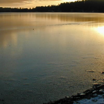 Pieni järvi auringonlaskun aikaan ohuessa jääpeitteessa alkutalvesta