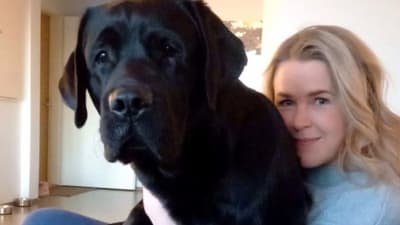 Hannah Norrena sitter i soffan och kramar om sin svarta labrador. Hunden sitter i hennes famn.