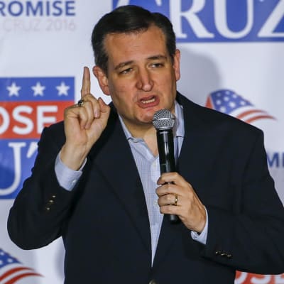 Ted Cruz puhuu mikrofoniin osoittaen oikean kätensä etusormella ylöspäin. Hänellä on tumma puku, kauluspaita mutta ei kravattia. Taustalla on Cruzin kampanjajulistetta.