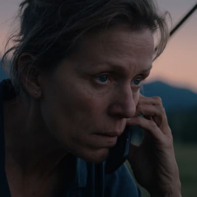 Mildred sitter och talar i sin mobil i ett öppet landskap.