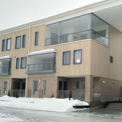 En fastighet med lokaler i flera våningar. Fasaden är i ljust trä. Marken är täckt av snö.