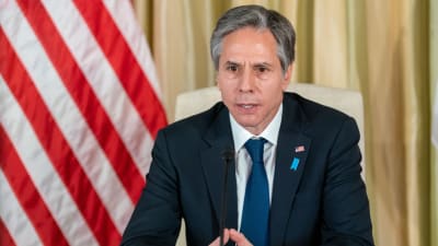 Antony Blinken, USA:s utrikesminister sitter vid ett bord och talar in i en mikrofon i samband med en presskonferens. I bakgrunden syns USA:s flagga.