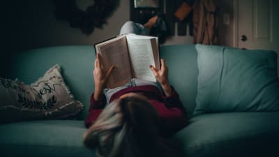 Kvinna ligger i en soffa och läser en bok.