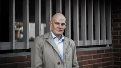 En bestämd man. I bakgrunden ett trästaket på en mur.