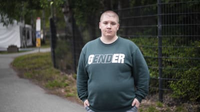 En allvarsam man står framför ett staket. På hans tröja står det "End gender".