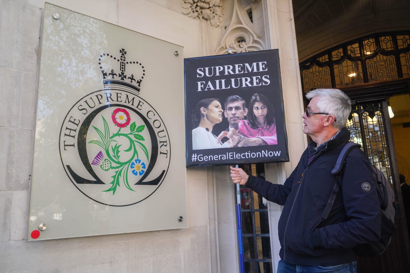 A protester with pictures of Prime Minister Rishi Sunak and former home secretaries Priti Patel and Suella Braverman outside the High Court in London.