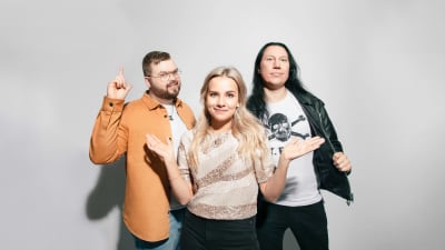 Tre personer som poserar framför en vit vägg. Seesar med glasögon, skägg, brunt hår och orange skjorta. Fanny med långt blont hår och glittrlig t-shorta. Kjell med långt svart hår, läderjacka och vit t-shorta med en dödsskalle.