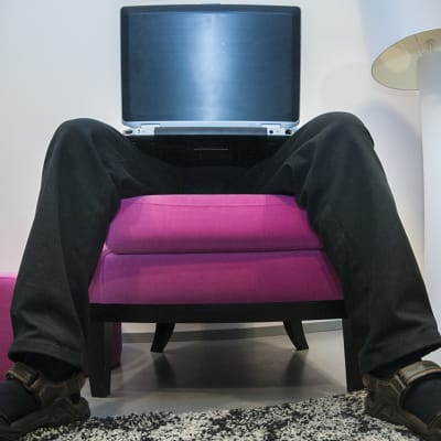 Mies istuu kannettava tietokone sylissään.