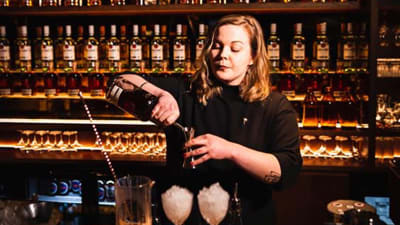 En bartender står vid en bar och häller upp två drinkar. 