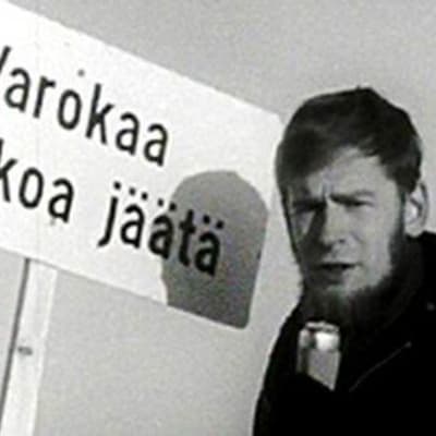 Yrjö Länsipuro Varokaa heikkoa jäätä -kyltin edessä.