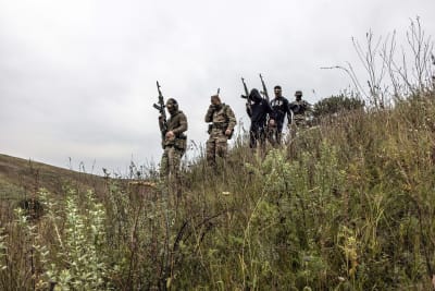 En grupp beväpnade män i terräng. En del av dem är klädda i camouflagedräkt, några i civila kläder.