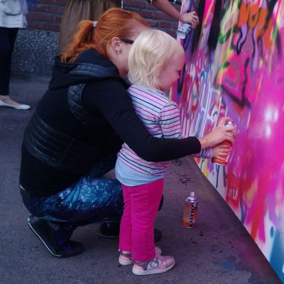 pieni tyttö maalaa seinää spraymaalilla äidin avustamana