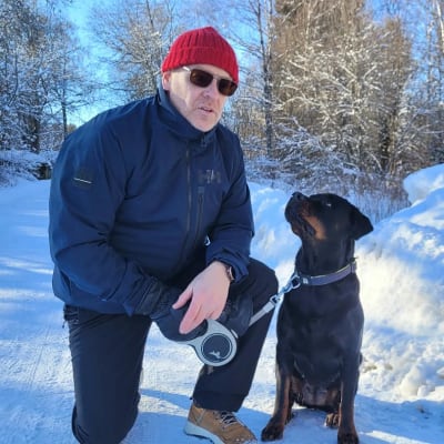 Mies ja hänen omistamansa Rottweiler-koira istuvat talvisessa pihassa ulkona