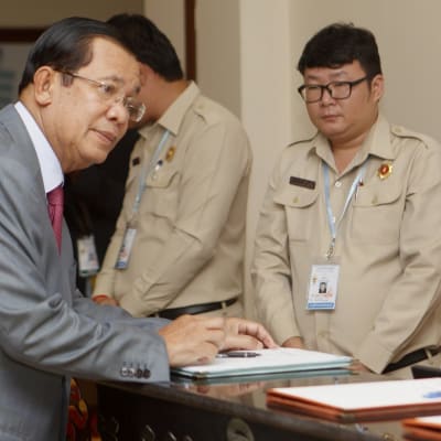 Hun Sen kansalliskokouksessa, kumartuu pöydän yli. 
