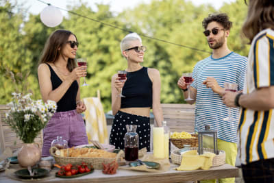 Ihmiset seisovat kesäisen piknikpöydän ääressä viinilasit käsissään.