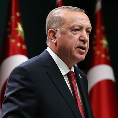 Turkiets president Recep Tayyip Erdoğan står framför en rad med turkiska flaggor.