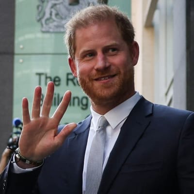 Prins Harry ser nöjd ut och vinkar med höger hand utanför en domstolsbyggnad.