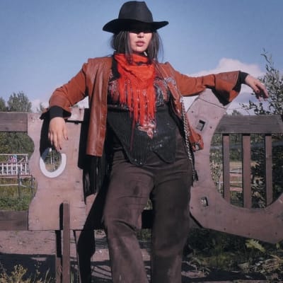 Stillbild av videoverk. Cowgirl-kvinna lutar mot staket.