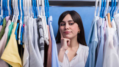 en vkinna står och tittar på kläder i en garderob
