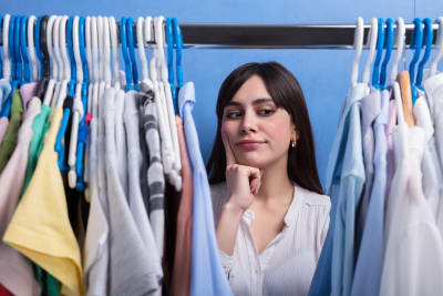 en vkinna står och tittar på kläder i en garderob
