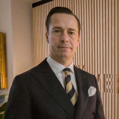 Carl Haglund står i Veritas kontor i Helsingfors iklädd mörk dubbelknäppt kavaj och slips . 