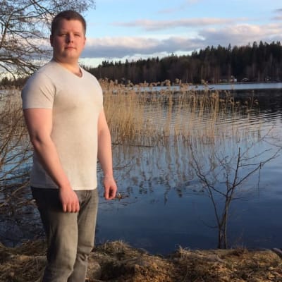 Ukko Kangasniemi seisoo järven rannassa ja katsoo kameraan.