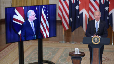 USA:s president Joe Biden vid ett podium i Vita huset medan Australiens premiärminister Scott Morrison syns på en tv-skärm bredvid honom.