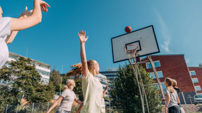 Tytöt pelaamassa koripalloa aurinkoisena päivänä
