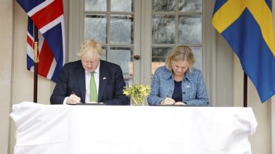 Boris Johnson och Magdalena Andersson sitter vid ett bord och skriver under var sitt dokument.