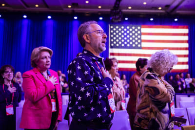 Flera personer står med högra handen på bröstet. Bakom dem syns en amerikansk flagga. 