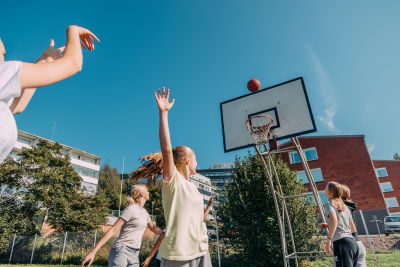 Tytöt pelaamassa koripalloa aurinkoisena päivänä