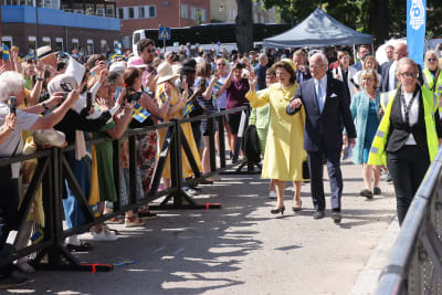 Kung Carl XVI Gustaf och drottning Silvia besöker Strängnäs. Folk i publiken viftar med svenska flaggor.