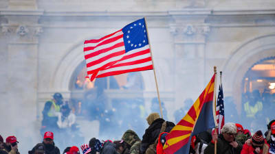 USA:s flagga vajar över en folkmassa framför kongressbyggnaden i Washington. Luften är dimmig av tårgas.