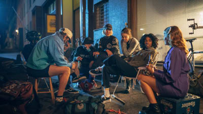 Ett gäng personer sitter i mörkret på en stadsgata under en paus i filminspelningen. 