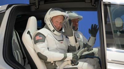 Astronauterna Douglas Hurley och Robert Behnken iklädda rymddräkter vinkar mot kameran.