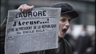 En pojke håller upp tidningen L'Aurore med löpsedelstexten: J'Accuse...!