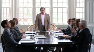På bilden ses ett ljust och pampigt mötesrum där sju personer sitter runt ett stort bord och i mitten syns en man som står upp.