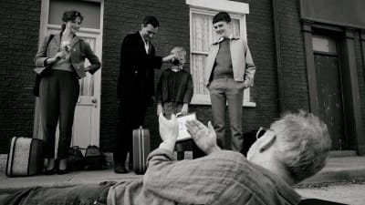 Elokuvan ohjaaja makaa kuvan alareunassa katsomassa kuvakulmaa ja näyttelijät seisovat talon vieressä.
