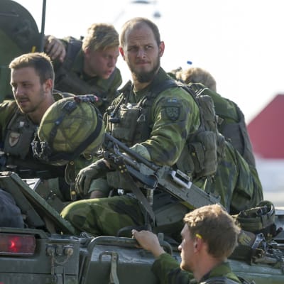 Kaksi ruotsalaista sotilasta istuu panssarivaunun päällä maastopuvuissa. Kolmas on maassa ja pitää kädellä kiinni vaunusta. 