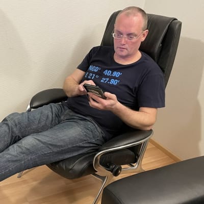 Vasaramäen Omakotiyhdistyksen puheenjohtaja Tomi Viitanen istuu nojatuolissa ja selaa kännykkää.