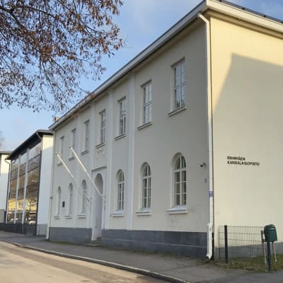 Vaaleankeltainen kaksikerroksinen Riihimäen kansalaisopiston rakennus kadun varressa syysauringossa.
