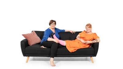 Veera ja Ulla istuvat rennosti sohvalla ja hymyilevät iloisesti.