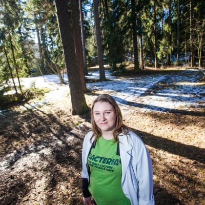 Alzheimertutkija Eloise Mikkonen seisoo puiden keskellä metsässä.