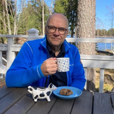 En man med en kaffemugg sitter nära havet.