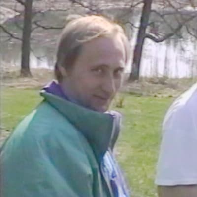 Vladimir Putin tittar rakt in i kameran, på en gräsmmatta, klädd i vindtygsjacka. 