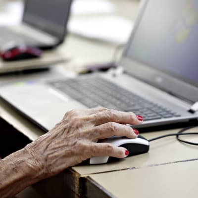 En hand som tillhör en äldre person håller i en datormus.