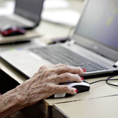 En hand som tillhör en äldre person håller i en datormus.