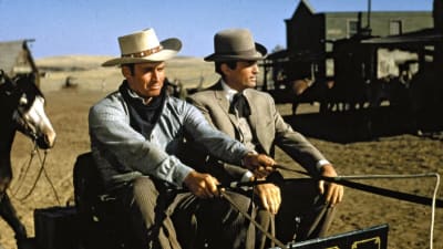 Kaksi miestä (Charlton Heston ja Gregory Peck) istuvat pienessä hevoskärryssä ajaen lännenkaupungin kadulla.
