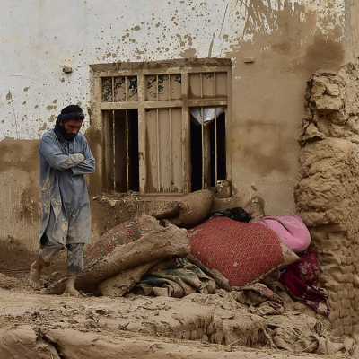 Två män i leriga kläder står utanför ett hus omringat av lera.
