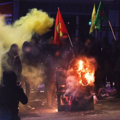 Mielenosoittajat polttavat presidentti Erdoganin kuvan. Mielenosoittajilla on myös lippuja kädessään. Ilmassa on savua.